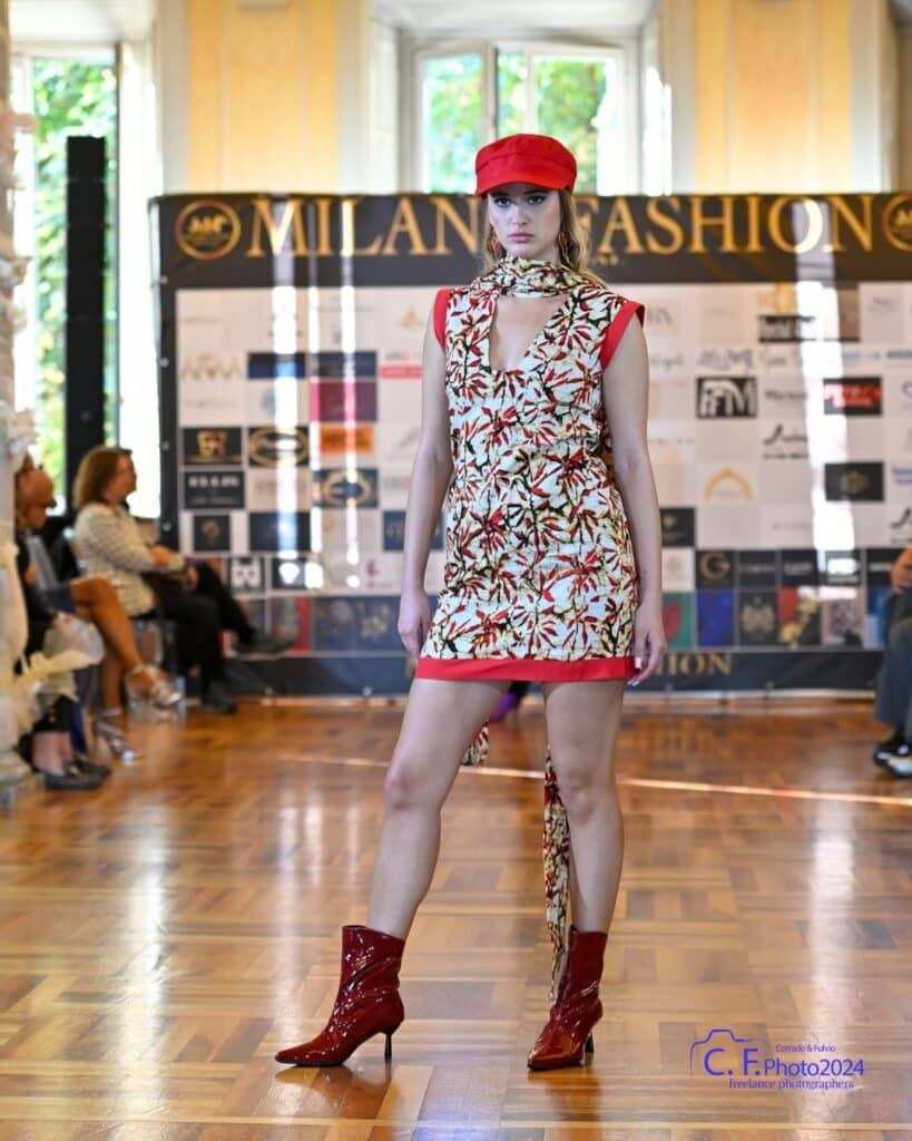 Runway model posing in a red cap and dress featuring batik fabric at Milano Fashion Official in Milan.