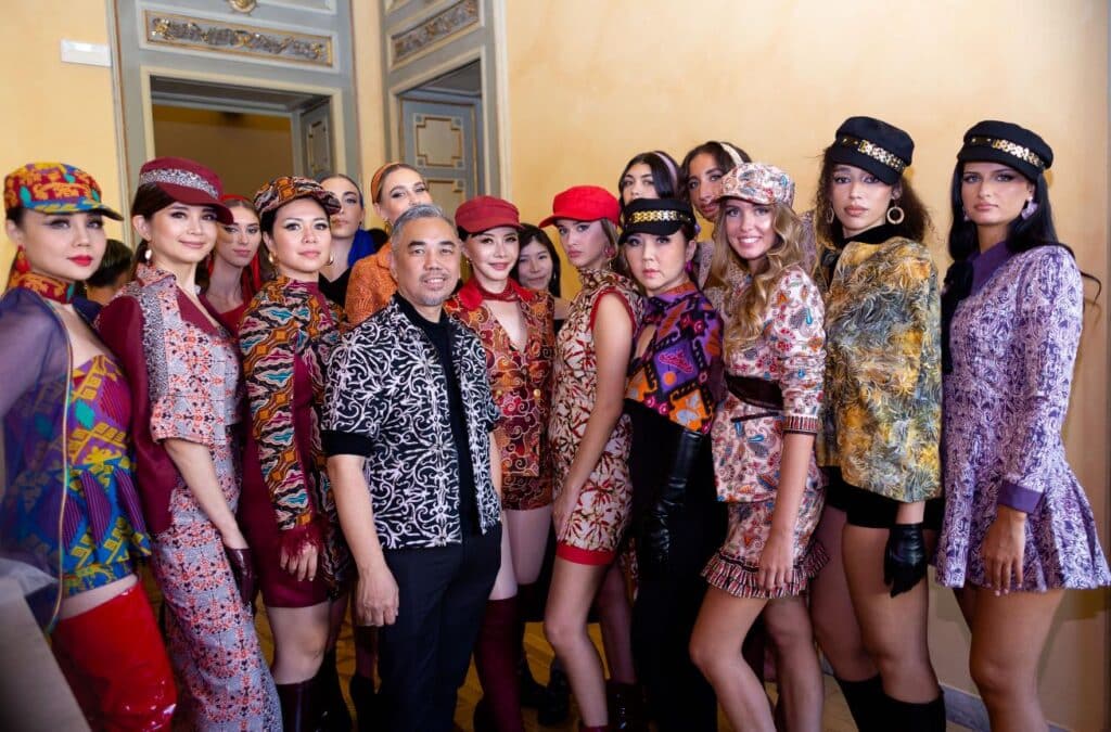 Karl Ho posing with runway models wearing colorful batik outfits at Milano Fashion Official in Milan.