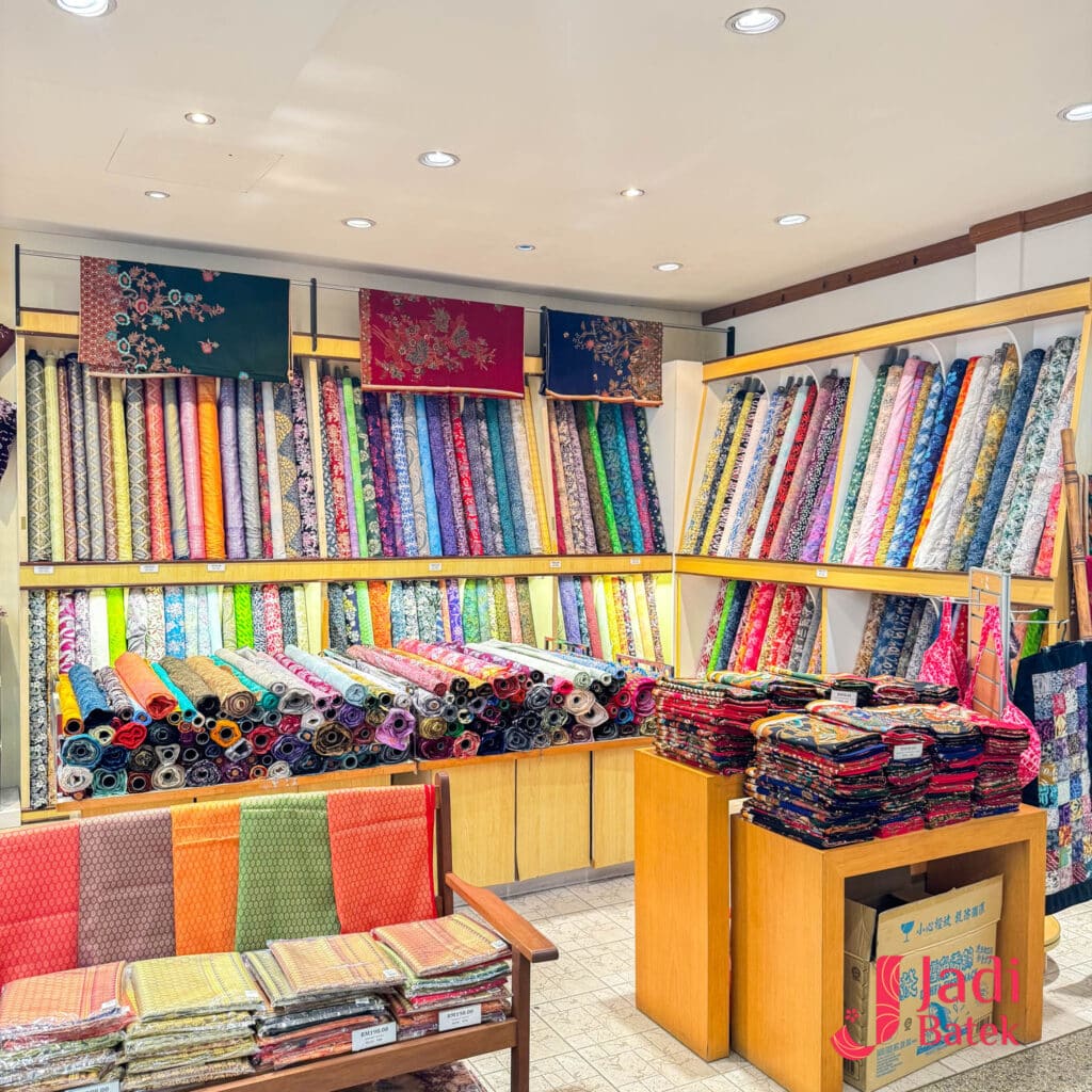 Batik fabric display shelves inside Jadi Batek gallery with colorful fabric rolls and folded textiles.