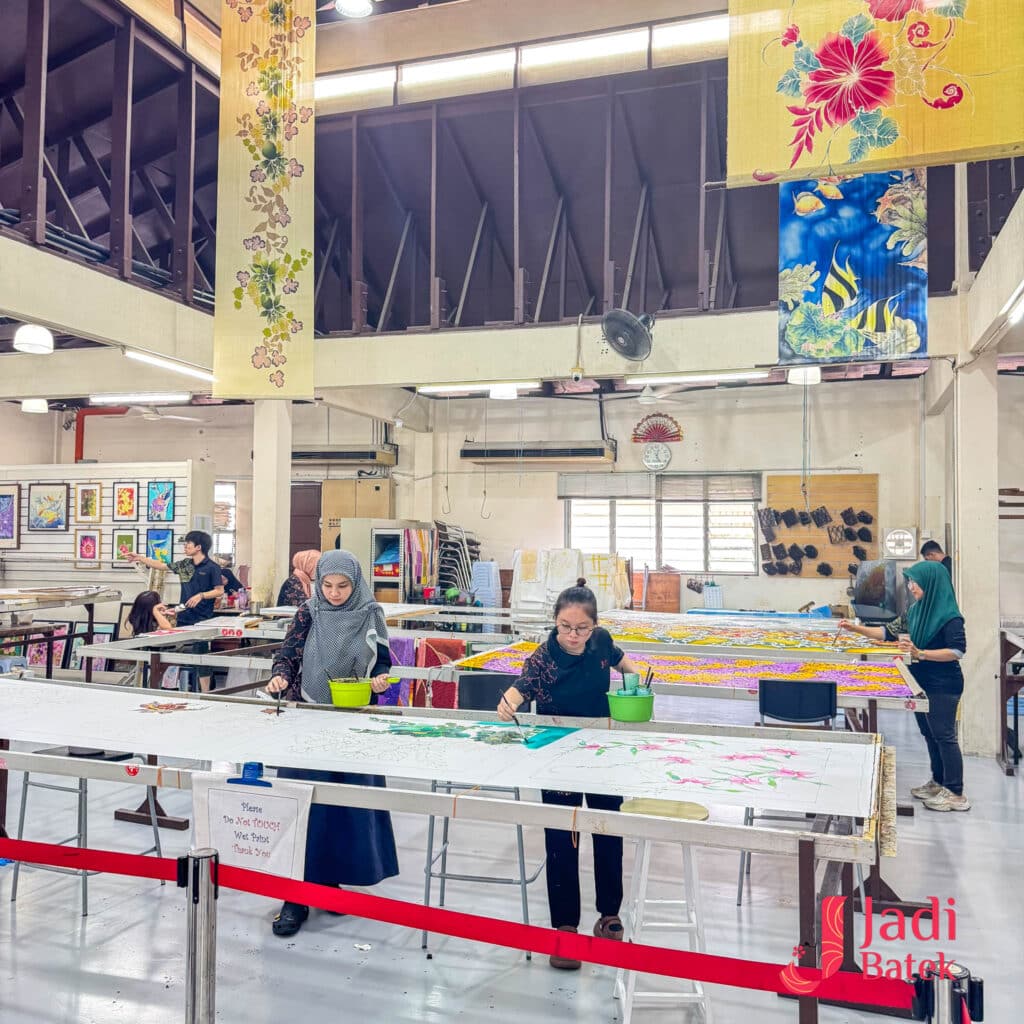 Jadi Batek in-house batik workshop with artisans working on large fabric tables in the studio.
