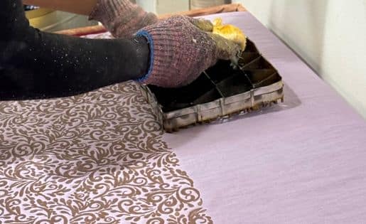 Artisan stamping a batik pattern onto fabric using a traditional copper block.